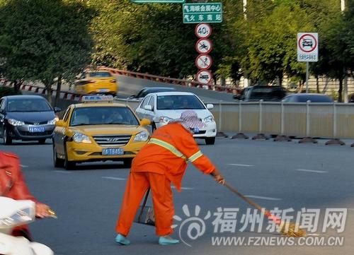 尤溪洲桥头,环卫工在车流中清除垃圾