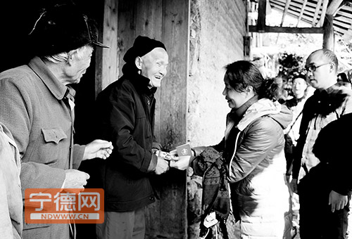 工作人员将残疾证与慰问金送到二老手中。