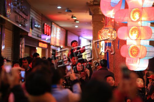 昨日，在泉州商城广场展区，一个小孩子骑在爸爸肩上看花灯