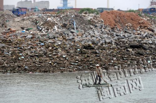 从海面向岸上看，可见海岸被成堆的建筑垃圾覆盖