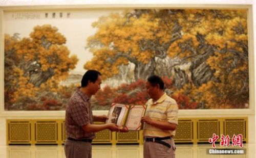 　6月20日，人民大会堂布置创作的国画作品《胡杨礼赞》正式亮相金色大厅中央位置。该作品由中央文史研究馆研究员张介宇和陕西省中国画院专职画家张国宏父子合作完成。图为张介宇、张国宏展示人民大会堂收藏证书。
