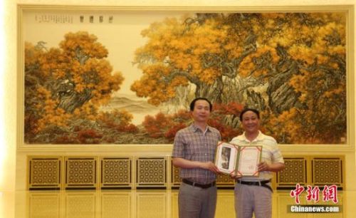 6月20日，人民大会堂布置创作的国画作品《胡杨礼赞》正式亮相金色大厅中央位置。该作品由中央文史研究馆研究员张介宇和陕西省中国画院专职画家张国宏父子合作完成。图为张介宇、张国宏展示人民大会堂收藏证书。中新社发 杨可佳摄