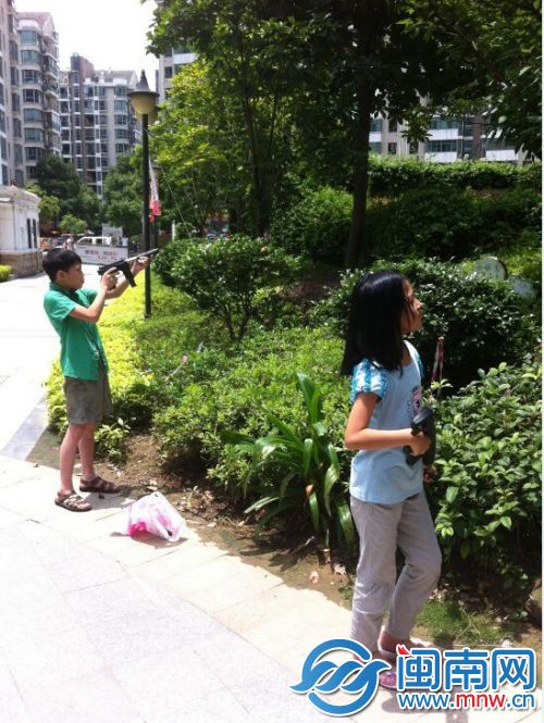 小孩用枪对着树打，旁边的红房子就是幼儿园