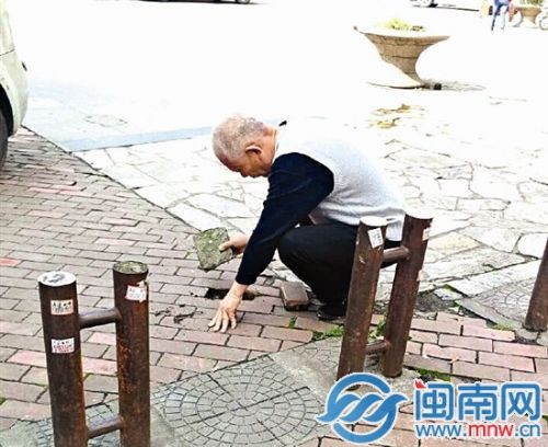 ▶老人蹲在地上，用石块把翘起的地砖补平（网友供图）