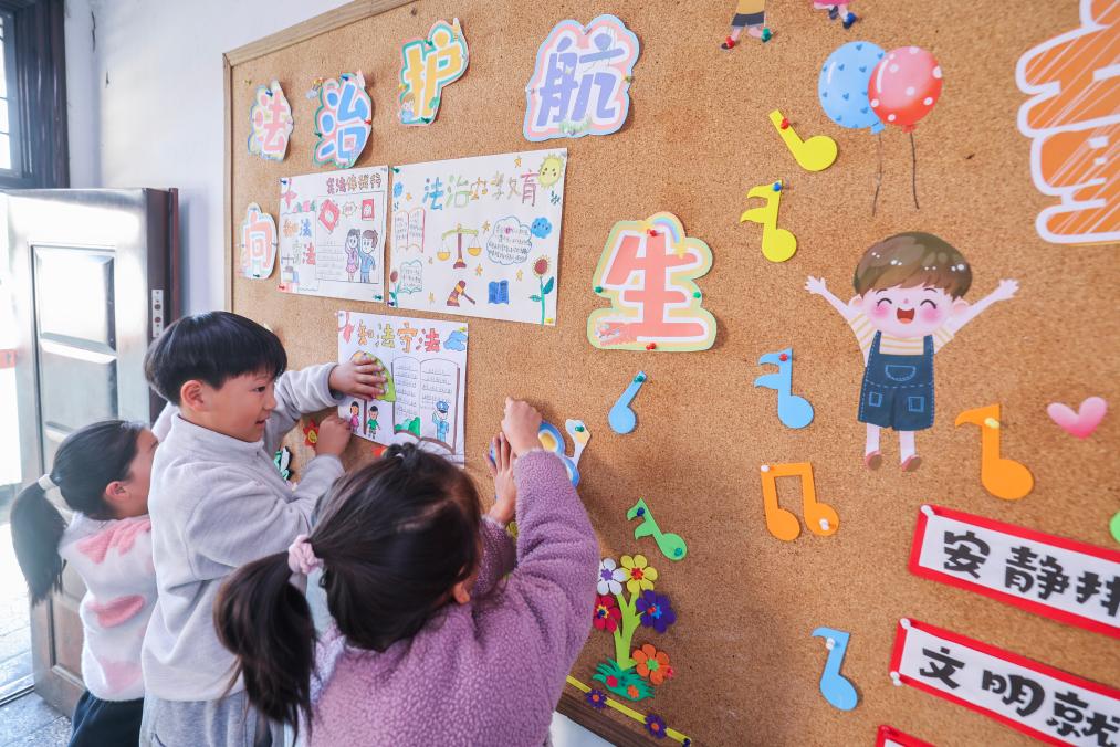 2025年12月9日,浙江省诸暨市暨南街道中心学校王家井小学的学生把自己创作的法治宣传画贴到教室的宣传栏中。新华社记者 徐昱 摄